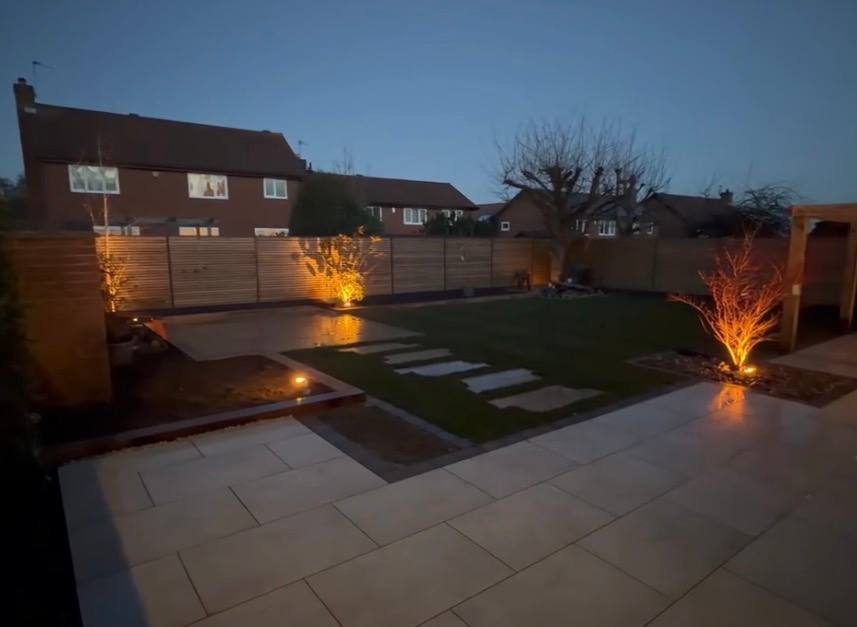 Garden at night with uplit trees, lit stepping stones and a porcelain patio
