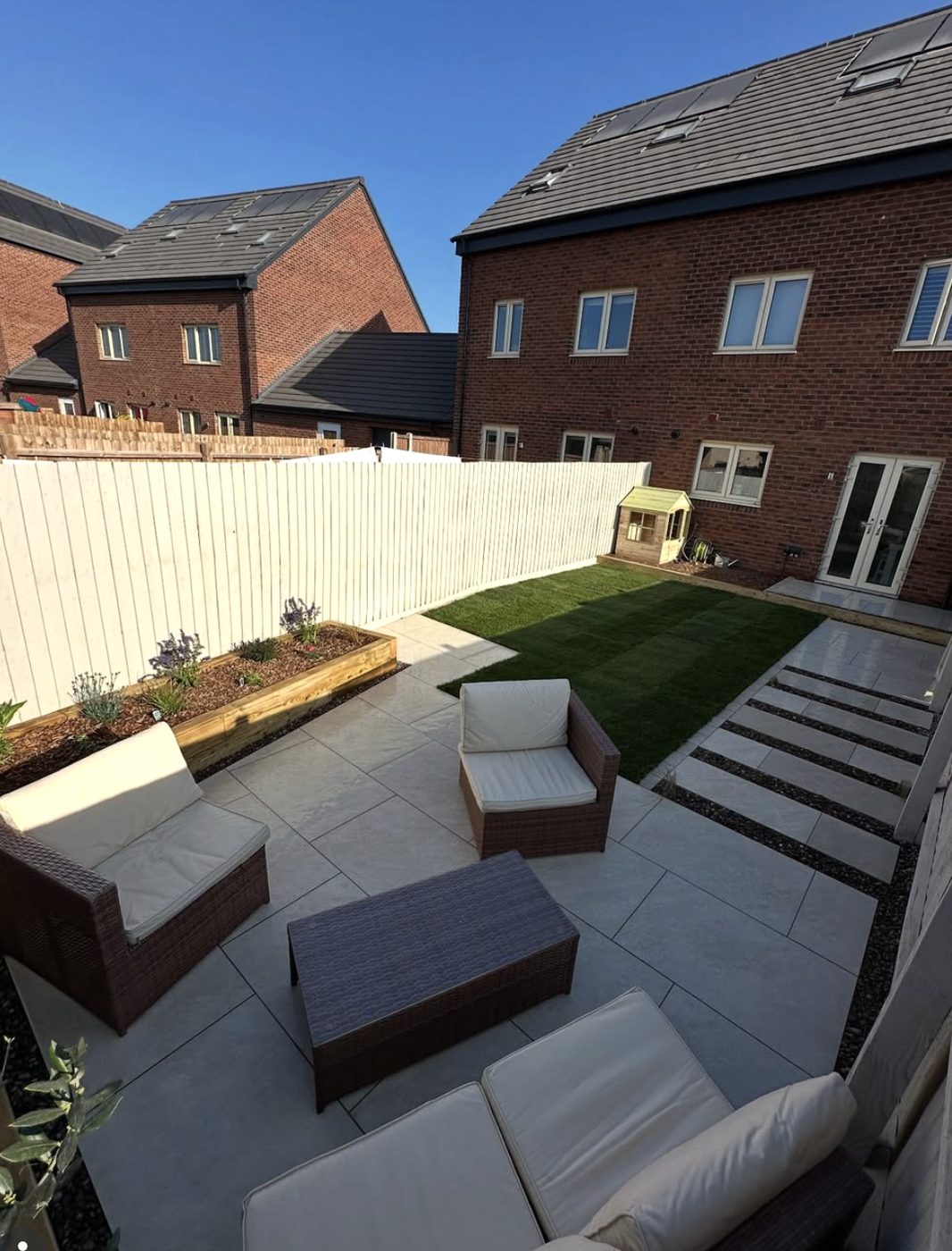 Porcelain patio with rattan furniture, stepping stones across a lawn and a sleeper raised bed