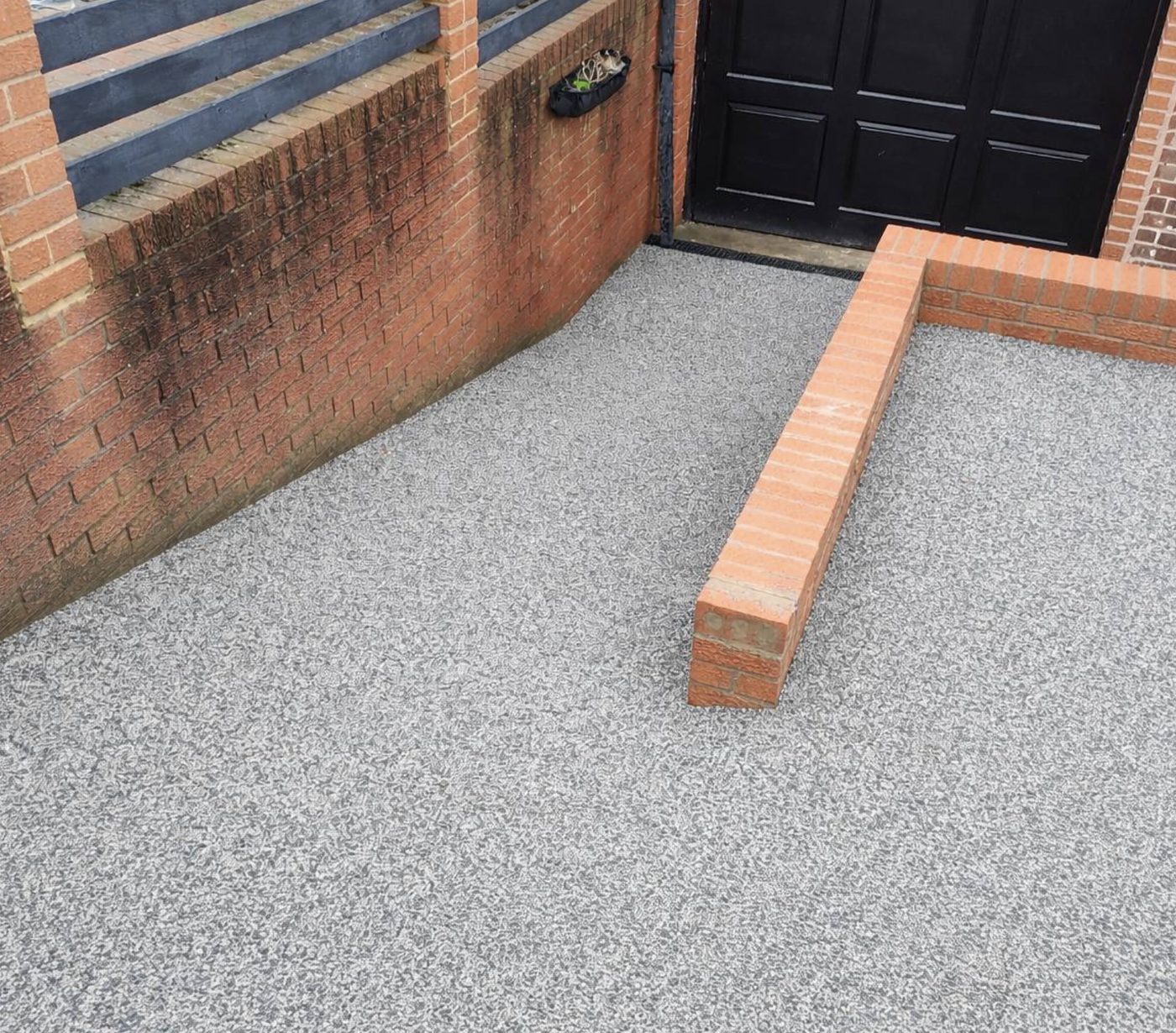 Grey resin bound driveway with red brick edging beside a garage