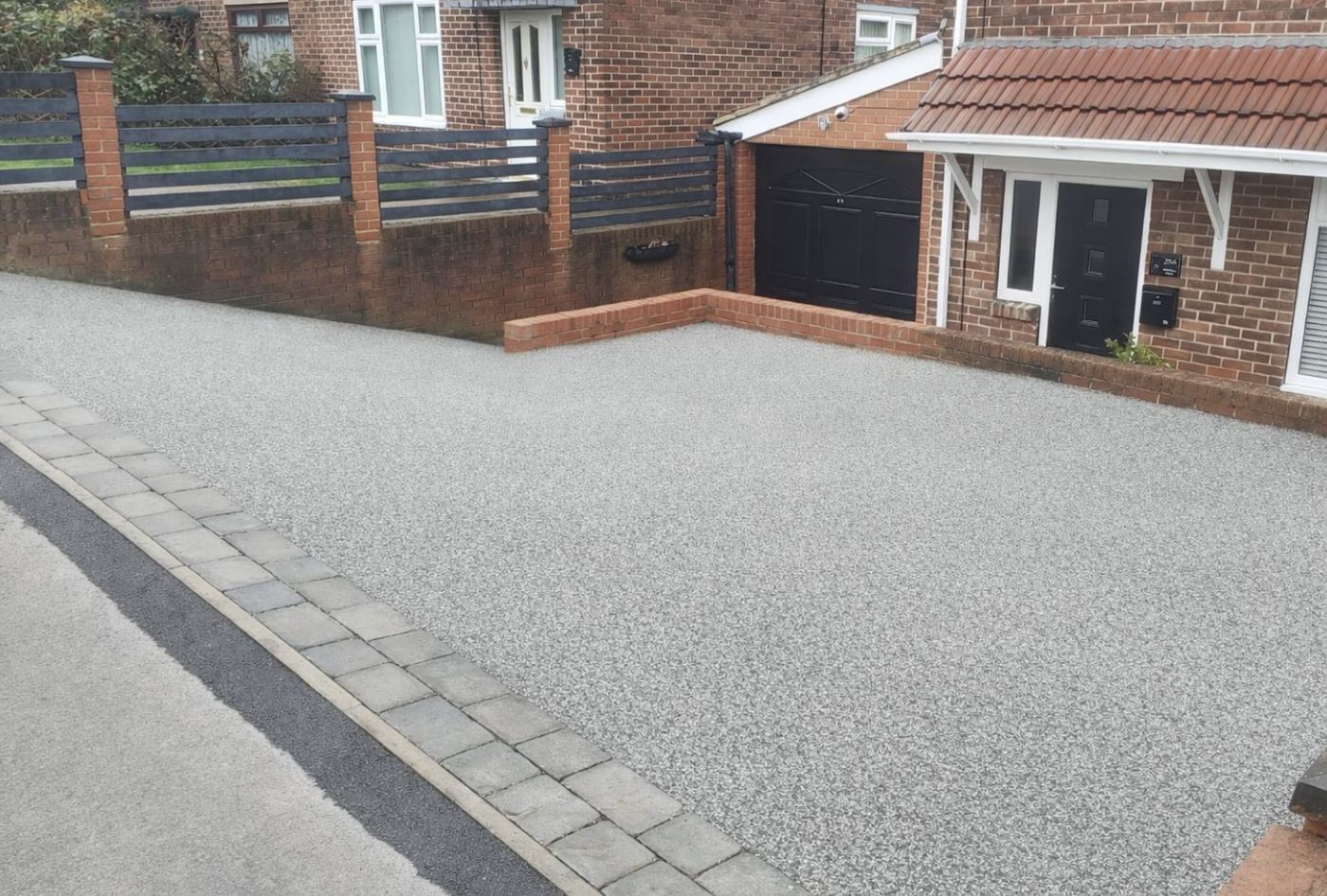 Wide resin bound driveway with a stone sett border in front of a house