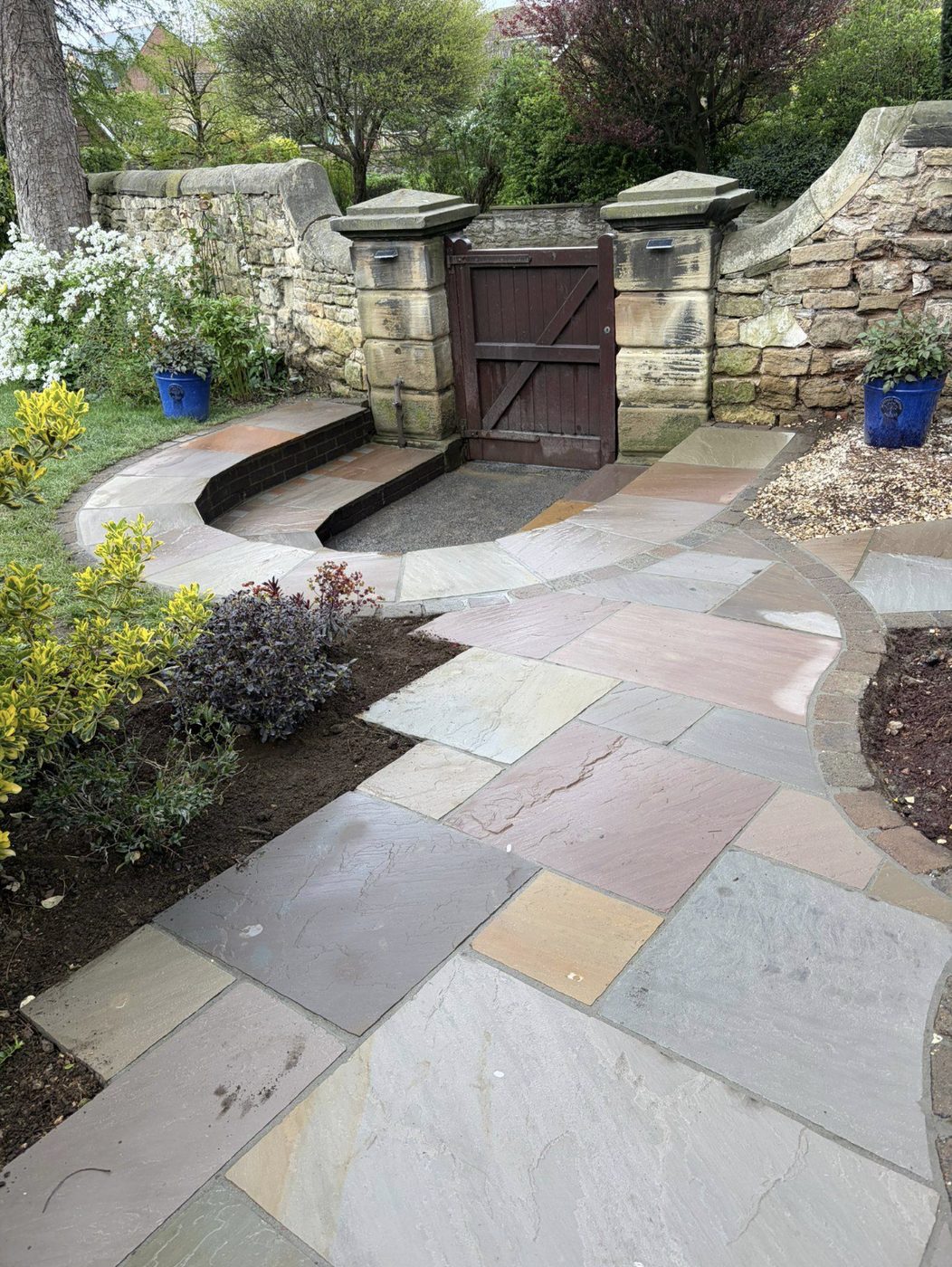 Indian sandstone garden paths curving to a gate between stone pillars